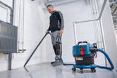 안전 장비를 착용한 사람이 무선 집진기를 사용하여 타일 바닥을 청소하고 있습니다.