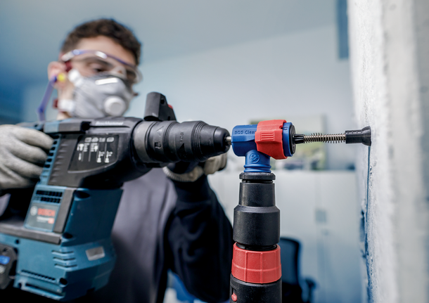 안전 장비를 착용한 사람이 해머 드릴을 사용하여 벽에 구멍을 뚫고 있습니다.