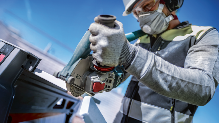 안전 장비를 착용한 사람이 야외에서 전동 공구를 사용하여 금속을 절단합니다.