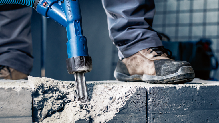 안전장비를 착용한 사람이 전동공구를 이용해 콘크리트를 깨고 있습니다.