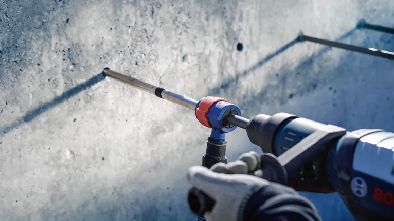 안전장비를 착용한 사람이 콘크리트 벽에 드릴을 박고 있습니다.