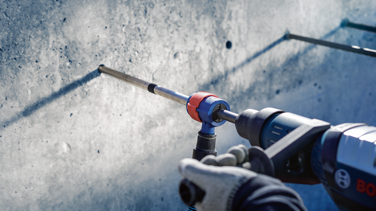 안전장비를 착용한 사람이 콘크리트 벽에 드릴을 박고 있습니다.