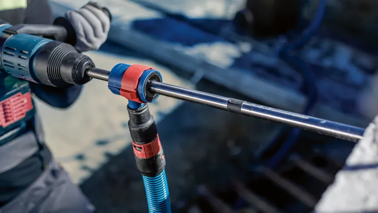 안전 장비를 착용한 사람이 회전 도구를 사용하여 콘크리트에 구멍을 뚫고 있습니다.