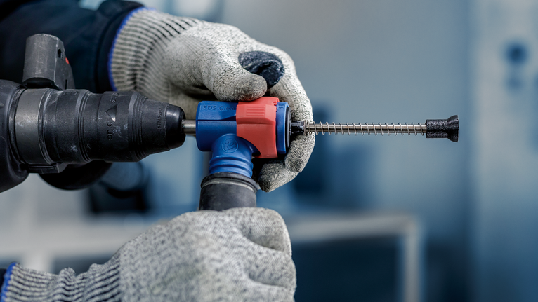 안전 장비를 착용하고, 끌 비트가 달린 회전 해머 드릴을 잡고 장갑을 낀 손.