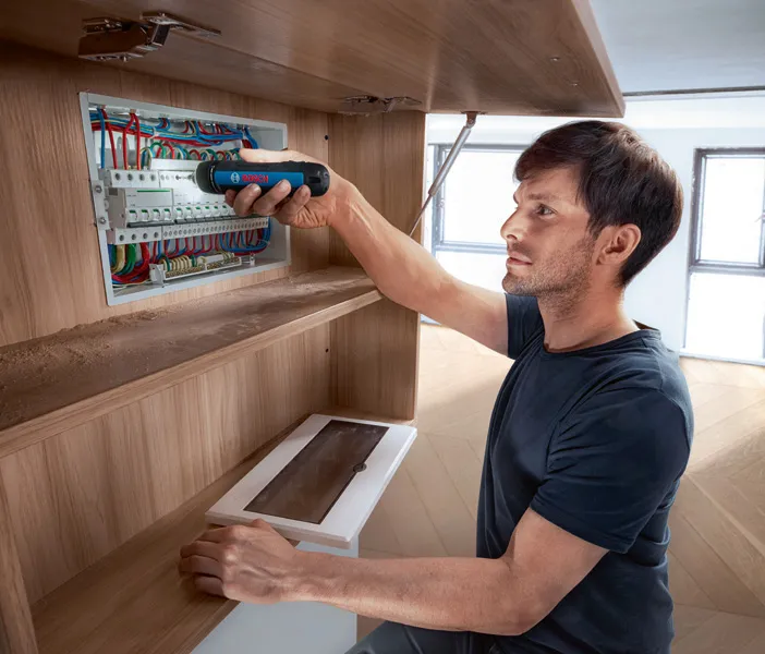 Bosch GO 한 사람이 무선 드라이버를 사용하여 전기 패널의 부품을 고정합니다.