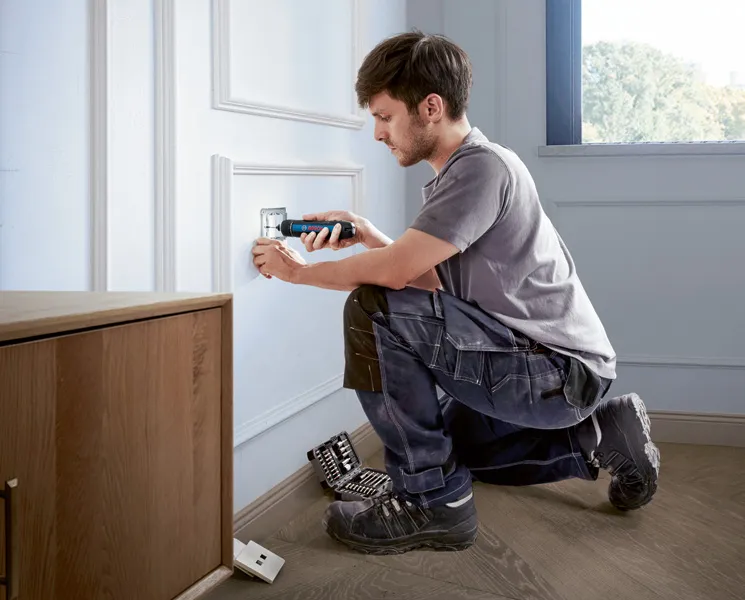 Bosch GO 한 사람이 무선 드라이버를 사용하여 전기 콘센트 커버를 설치하고 있습니다.