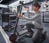 한 사람이 작업장에서 무선 드라이버를 이용해 전기 스쿠터를 수리하고 있다.