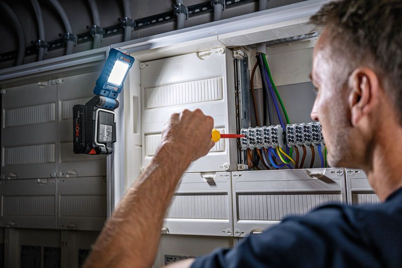 GLI 18V-800 한 사람이 전기 패널에 드라이버를 사용하고, 조명을 위해 무선 전구를 부착했습니다.