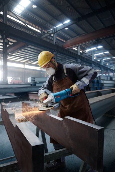 GWS 27-230 JR 안전장비를 착용한 사람이 큰 금속 기둥을 갈아서 불꽃을 낸다.