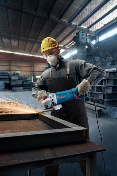 GWS 27-230 JR 안전 장비를 착용한 사람이 공장에서 금속을 갈아서 불꽃을 일으킨다.