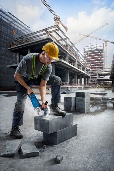 안전장비를 착용한 사람이 건설 현장에서 콘크리트 블록을 자르고 있습니다.