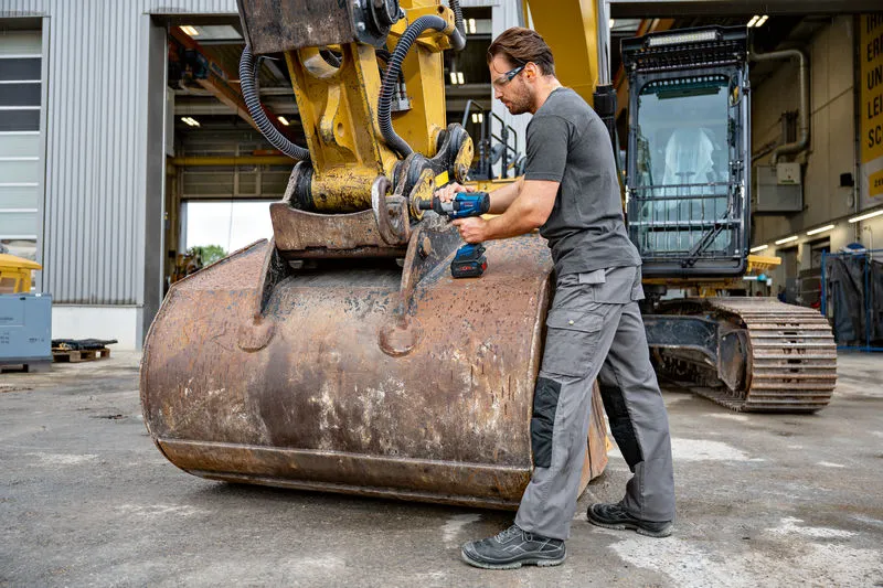 안전 장비를 착용한 사람이 중장비에 충격 렌치를 사용하고 있습니다.