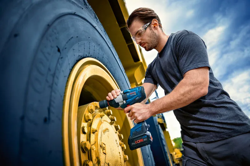 안전장비를 착용한 사람이 대형 차량 바퀴에 임팩트 렌치를 사용하고 있습니다.