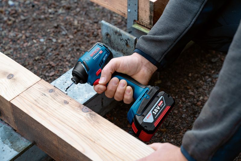 한 사람이 무선 드릴을 사용해 나무 들보에 나사를 박고 있습니다.