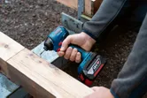한 사람이 무선 드릴을 사용해 나무 들보에 나사를 박고 있습니다.