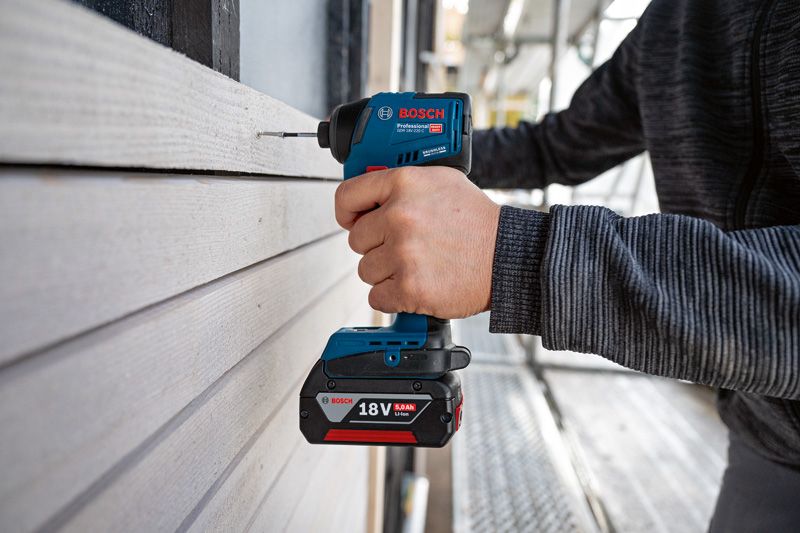 한 사람이 무선 전동 드릴을 사용하여 목재 사이딩에 구멍을 뚫고 있습니다.