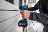 한 사람이 무선 전동 드릴을 사용하여 목재 사이딩에 구멍을 뚫고 있습니다.