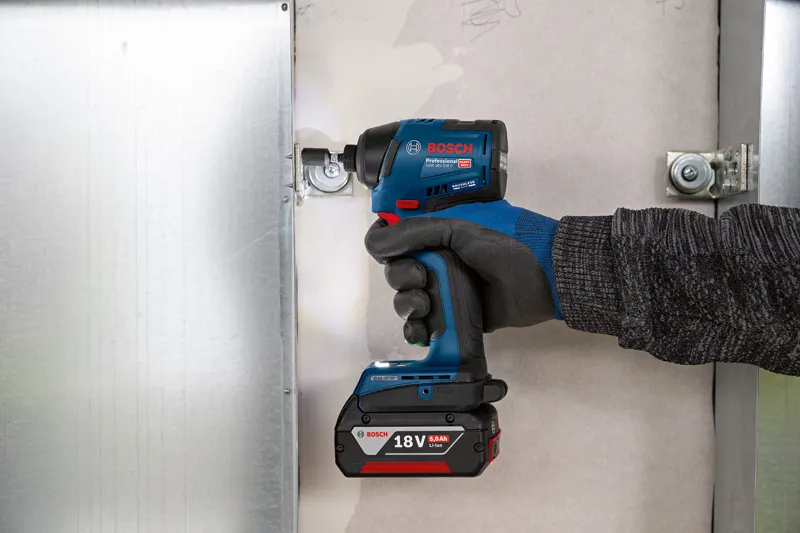 안전 장비를 착용한 사람이 무선 충격 드라이버를 사용하여 금속 프레임을 고정합니다.