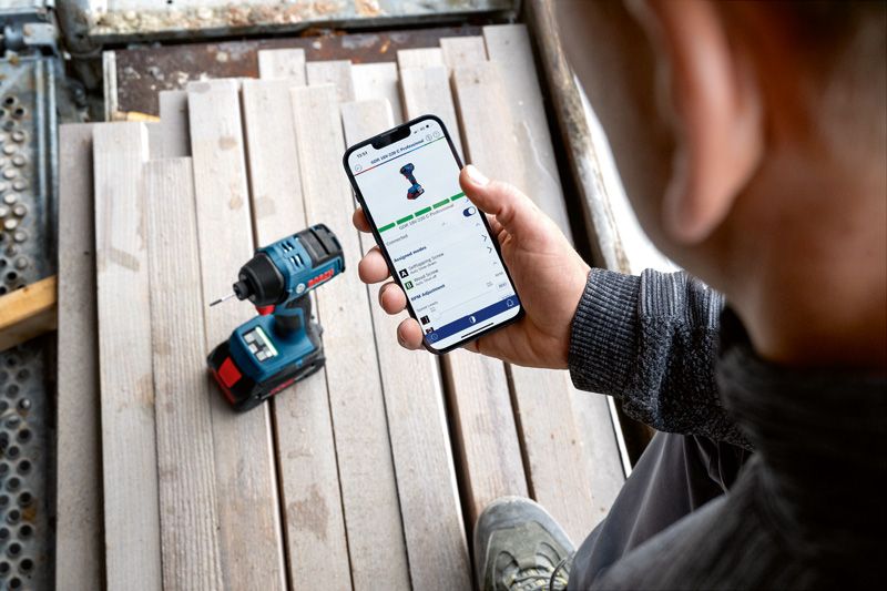 한 사람이 무선 드릴 근처에서 스마트폰으로 전동 공구의 앱 기능을 확인하고 있습니다.