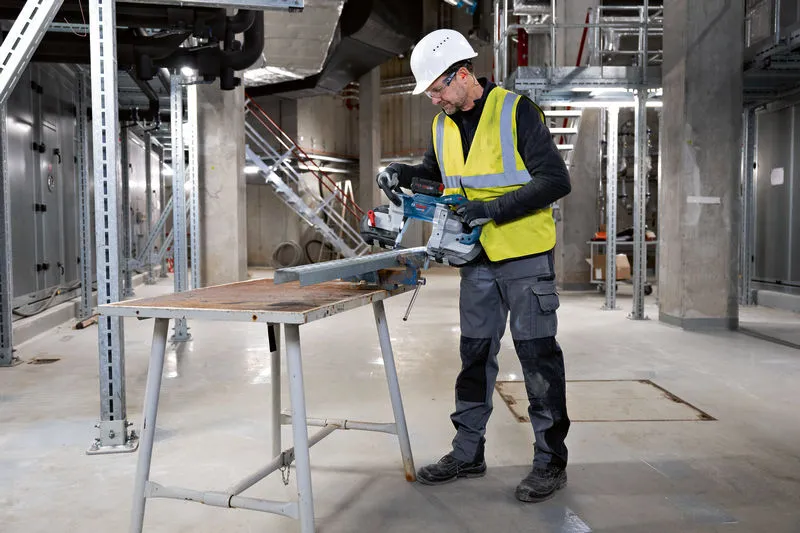 안전 장비를 착용한 사람이 무선 밴드톱으로 금속 빔을 자릅니다.