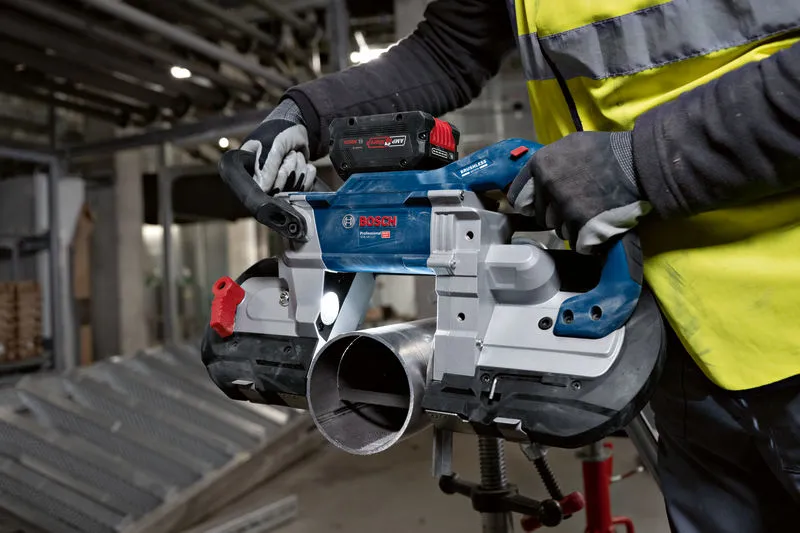 안전 장비를 착용한 사람이 무선 밴드톱을 사용하여 금속 파이프를 절단하고 있습니다.