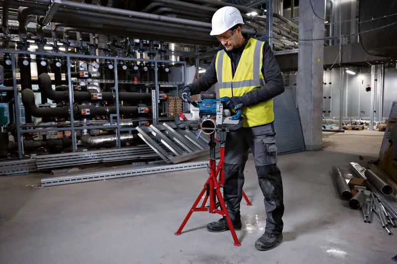 안전 장비를 착용한 사람이 무선 밴드톱을 사용하여 금속 파이프를 절단하고 있습니다.