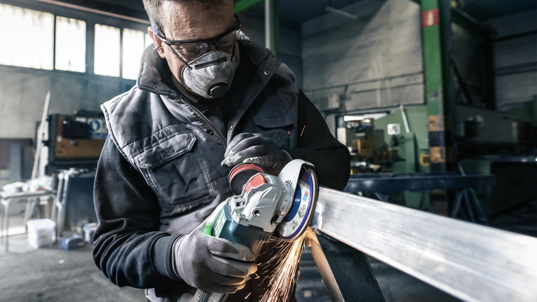 PRO X571 플랩 디스크, 직선, 125mm, G40, X-Lock 안전 장비를 착용한 사람이 금속 막대를 갈아서 불꽃을 낸다.