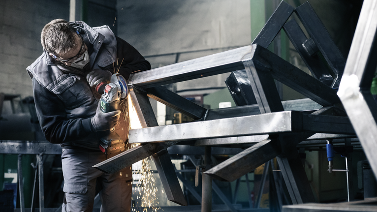 PRO X571 플랩 디스크, 직선, 125mm, G40, X-Lock 안전 장비를 착용한 사람이 금속 프레임을 갈아서 불꽃이 난다.