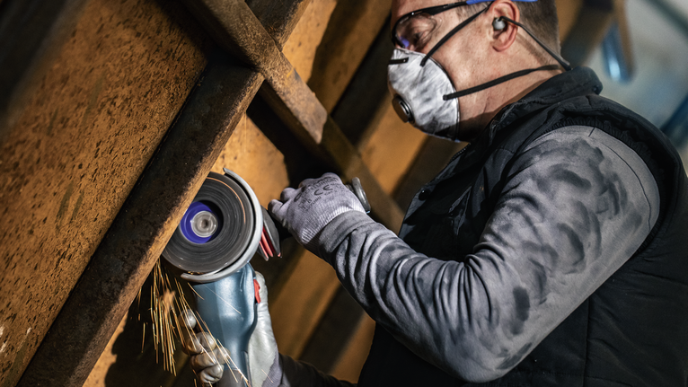 PRO N377 클리닝 디스크, 125mm, 22.23mm, X-Lock 안전 장비를 착용한 사람이 휴대용 분쇄기로 금속을 자릅니다.