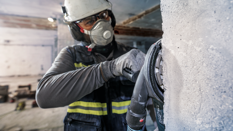 PRO Concrete 연마 헤드, 50 x 125mm, 22.23mm 안전 장비를 착용한 사람이 전동 공구로 콘크리트 벽을 갈고 있습니다.