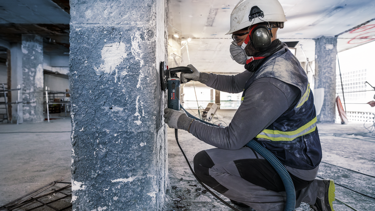 PRO Concrete 연마 헤드, 50 x 125mm, 22.23mm 안전 장비를 착용한 사람이 건설 현장에서 콘크리트 기둥을 갈아내고 있습니다.