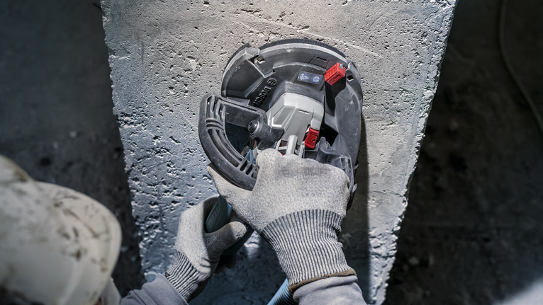 안전 장비를 착용한 사람이 전동 공구로 콘크리트를 갈아내고 있습니다.