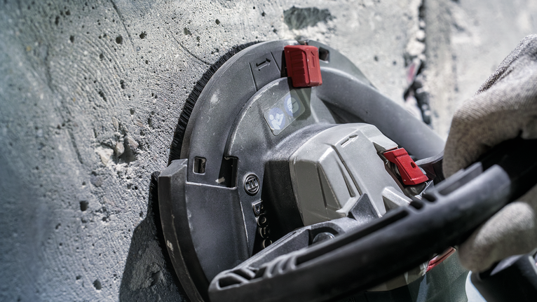 안전 장비를 착용한 사람이 전동 공구로 콘크리트 벽을 갈고 있습니다.