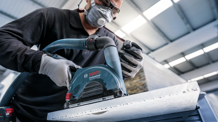 안전 장비를 착용한 사람이 전동 공구로 콘크리트 표면을 연마하고 있습니다.