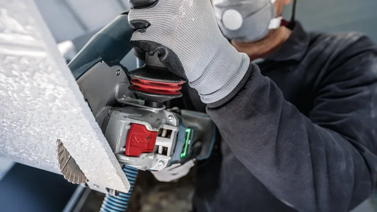 안전 장비를 착용한 사람이 전동 공구로 패널을 자릅니다.