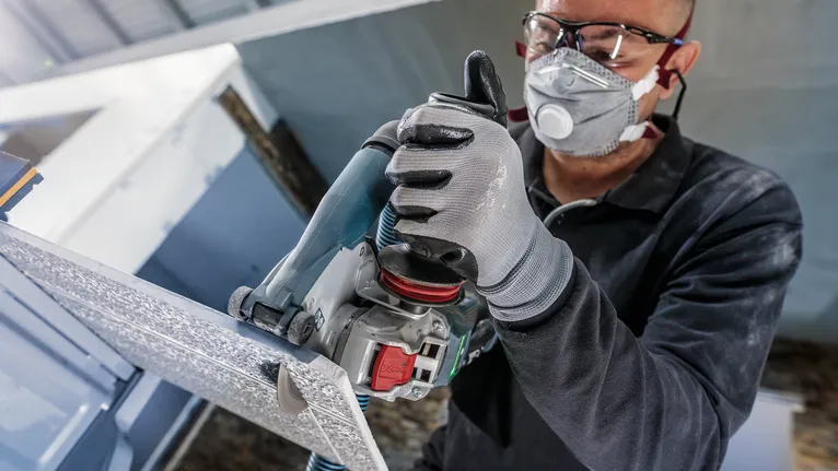 안전 장비를 착용한 사람이 전동 공구로 금속 패널을 자릅니다.