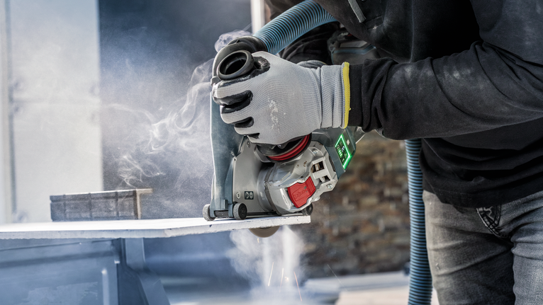 안전장비를 착용한 사람이 전동 절단기를 사용하여 돌판을 자르고 있습니다.