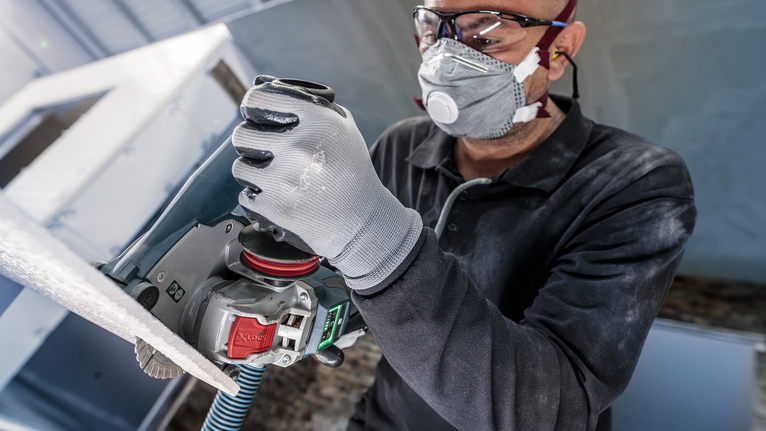 안전 장비를 착용한 사람이 전동 공구를 사용하여 표면을 연마하고 있습니다.