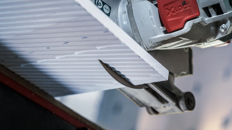 PRO Ceramic X-Lock 다이아몬드 디스크, 125 x 22.23mm, 22.23mm 원형 톱으로 질감이 있는 타일 패널을 가까이서 절단하는 모습입니다.