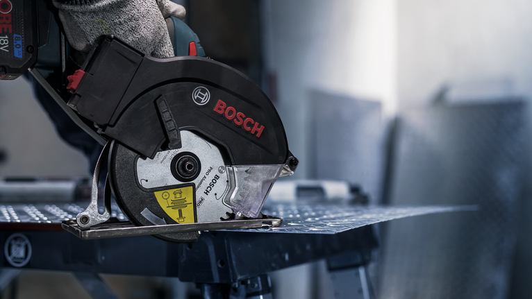 안전 장비를 착용한 사람이 원형 톱으로 금속판을 자릅니다.