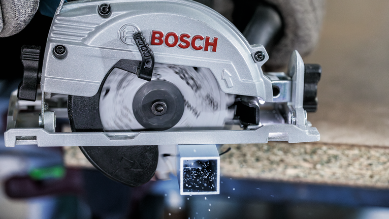 안전 장비를 착용한 사람이 원형 톱을 사용하여 금속 사각형 튜브를 자릅니다.