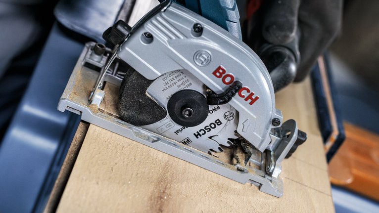 안전 장비를 착용한 사람이 원형 톱을 사용하여 나무를 자릅니다.