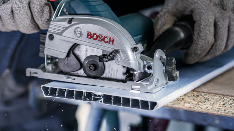 안전 장비를 착용한 사람이 원형 톱으로 금속판을 자릅니다.