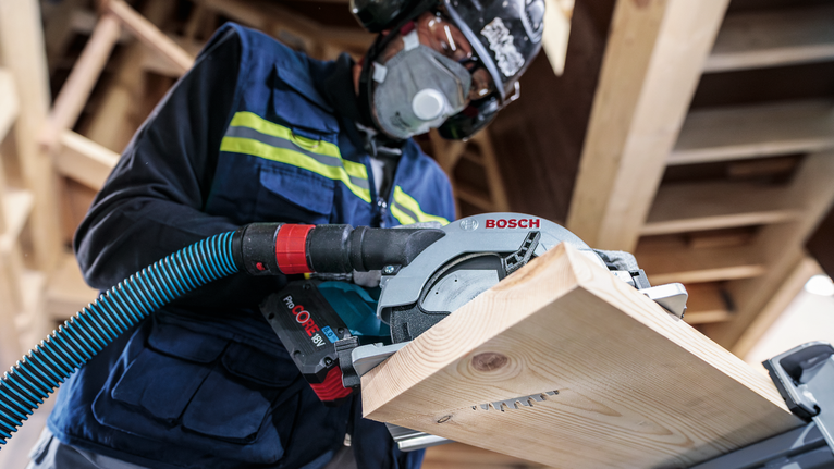 PRO Wood cordless 원형 톱날, 85 x 1.1 x 15mm 안전 장비를 착용한 사람이 원형 톱으로 나무 판자를 자릅니다.