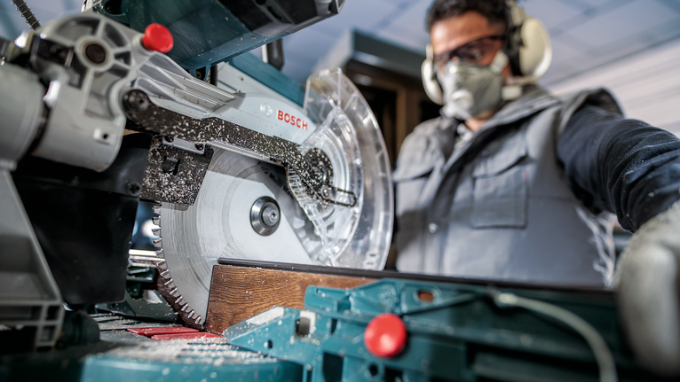 안전 장비를 착용한 사람이 원형 톱을 사용하여 나무 판자를 자릅니다.