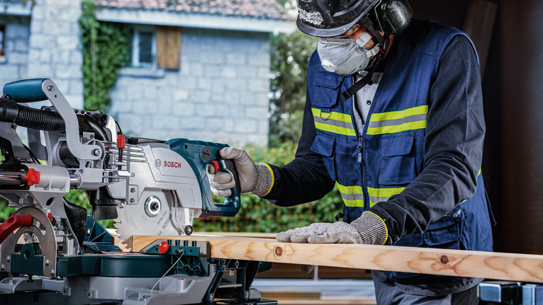 PRO Wood cordless 원형 톱날, 254 x 2.2 x 30mm, T24 안전 장비를 착용한 사람이 마이터 톱으로 나무 판자를 자르고 있습니다.