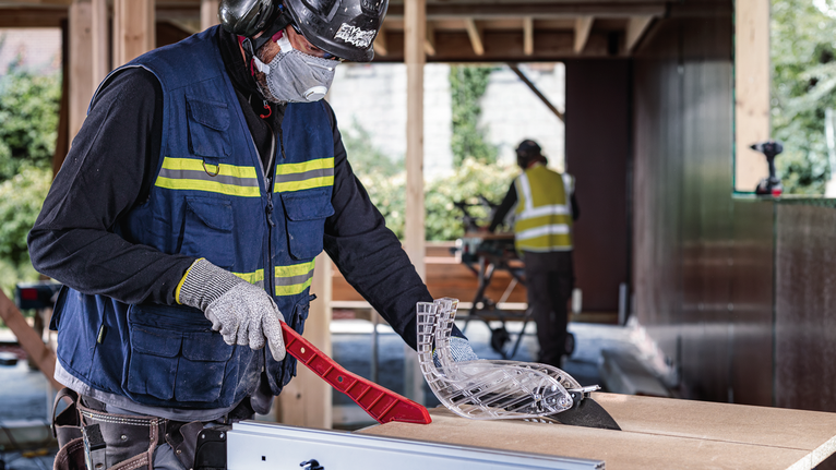 안전 장비를 착용한 사람이 건설 현장에서 톱날 보호대를 조정하고 있습니다.
