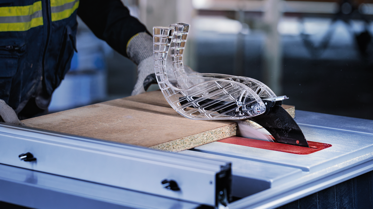 작업장에서 안전 장비를 착용한 사람이 테이블 톱을 통해 목재를 안내하고 있습니다.