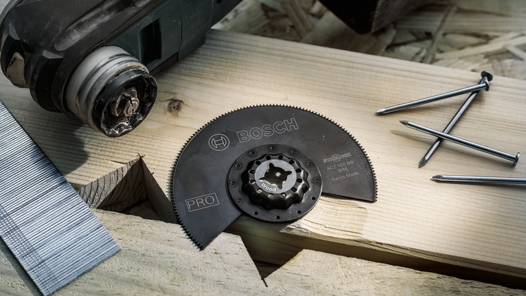 PRO ACZ 100 BB 멀티커터 날, 100mm 나무를 자르기 위한 원형 톱날 부착물을 근처에 못이 박힌 나무판 위에 올려놓았습니다.