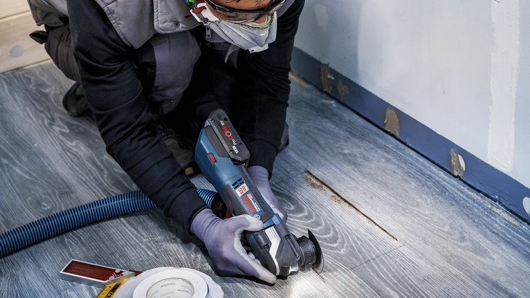 안전 장비를 착용한 사람이 전동 공구로 나무 바닥을 자르고 있습니다.